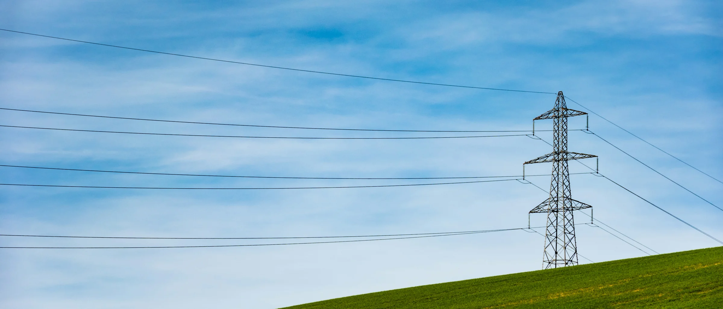 Słup kratowy z linią energetyczną nad zielonym wzniesieniem